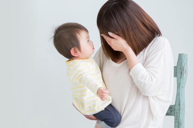 赤ちゃんを抱えながら手で顔を覆う母親