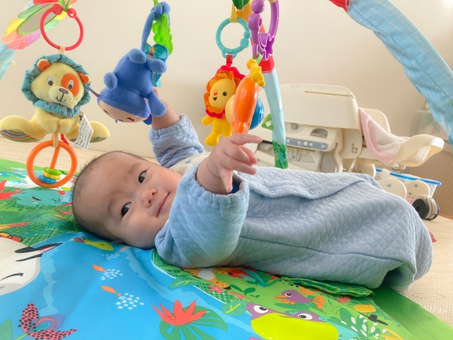 ベビージムのおもちゃをつかんで微笑む赤ちゃん