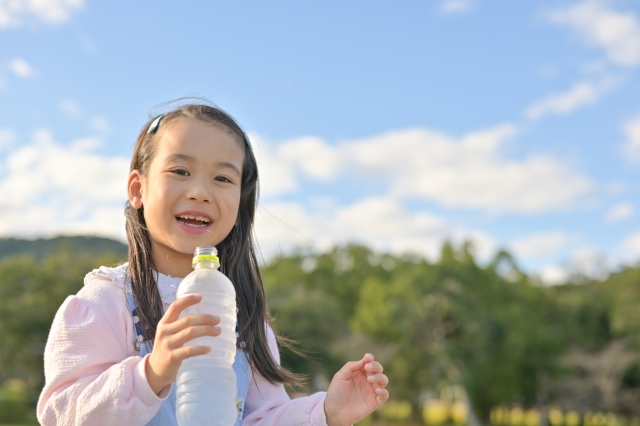 外でペットボトルの水を飲む女の子