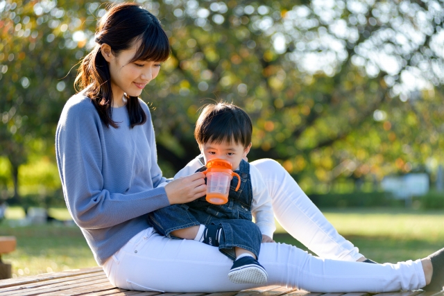 外で母親が息子に赤ちゃん用マグで飲み物を与えている